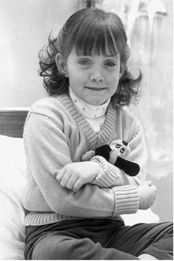Jennifer at age seven, seated and holding a small stuffed dog